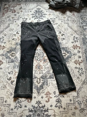 Svarta flared 4 leafs jeans - Unika svarta jeans med vita färgstänk och patchade knän. Raka ben och flera fickor både fram och bak ger en cool och avslappnad vibe. Perfekta för dig som gillar streetwear och vill sticka ut lite extra.