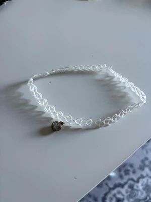 Vit choker med liten berlock - Säljer en vit choker i plast med spiralformad design och en liten rund berlock med glittrande sten. Halsbandet har en enkel och trendig look som passar perfekt till olika stilar.