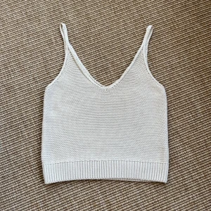 Beige stickad linnetopp från Dobber - Beige stickat linne från Dobber i stl XS, i bomull och normal i storleken. Smala axelband och ribbad kant nedtill.. 100% bomull. Oanvänd med prislapp. 