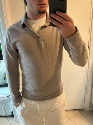 Beige stickad tröja med krage - Säljer en stilren beige stickad tröja från Oscar Jacobson. Tröjan har klassisk krage, knäppning vid halsen och långa ärmar. Perfekt för dig som gillar en clean och avslappnad look. Materialet känns mjukt och följsamt. Krympt från storlek M till ca S/XS
