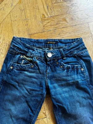 Blå bootcut jeans med låg midja - Snygga blå bootcut jeans med låg midja och bootcut från Killah. Jeansen har slitningar och en cool tvättad look. Perfekta för en avslappnad stil och passar till det mesta. Stängs med knapp och dragkedja.