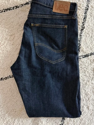 Mörkblå Lee Luke jeans W33 L30 - Snygga mörkblå jeans från Lee, modell Luke. Klassisk femficksdesign med Lee-läderpatch bak i midjan. Jeansen har raka ben och är tillverkade i slitstarkt denimtyg. Har vuxit ur dem och knappt använda.