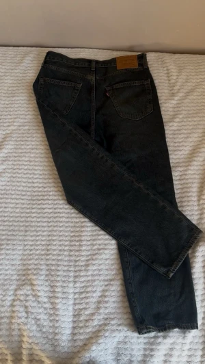 Levi's svarta/mörk blåa jeans 568 - Säljer ett par svarta Levi's 568 jeans med en relaxed passform och klassiska bakfickor. Jeansen har en vintage look, tydliga sömmar och är tillverkade i slitstark denim. Lite lätt i dragkedjan, annars helt perfekta för dig som gillar tidlös stil och vill ha ett par ikoniska jeans. 