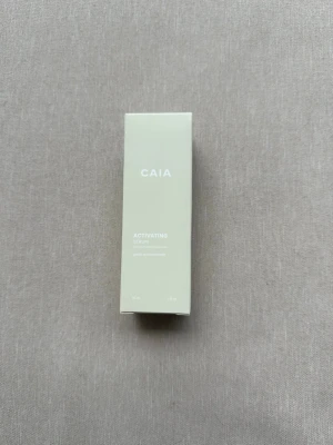 CAIA Activating Serum 30ml - Säljer ett CAIA Activating Serum i en stilren ljusbeige förpackning. Serumet kommer i en 30 ml kartong och är perfekt för dig som vill boosta din hudvårdsrutin med extra glow och återfuktning. Förpackningen är oöppnad och plomberad