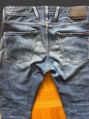 Blå Replay jeans med raka ben - Snygga blå jeans från Replay med klassisk femficksdesign och raka ben. Jeansen har en ljus tvätt och diskreta slitningar för en avslappnad look. Tillverkade i mjuk denim med läderpatch bak i midjan och detaljerade sömmar på bakfickorna.