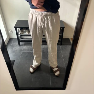 Beiga linnebyxor med resårmidja - Säljer ett par beiga linnebyxor med avslappnad passform och resår i midjan. Byxorna har raka ben och sidofickor, perfekta för en chill och stilren look. Materialet är lätt och luftigt linne, vilket gör dem sköna att bära under varmare dagar. De är helt oanvända