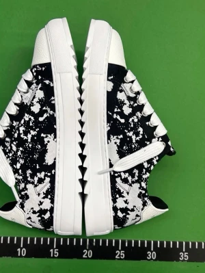 Numeris skor - Svarta och vita sneakers från Numeris med unik splattermönstrad canvas och vita detaljer. Skorna har vita snören, grov sula med taggig kant och Numeris-logga på hälen. Perfekta för dig som vill sticka ut med en cool och modern stil.