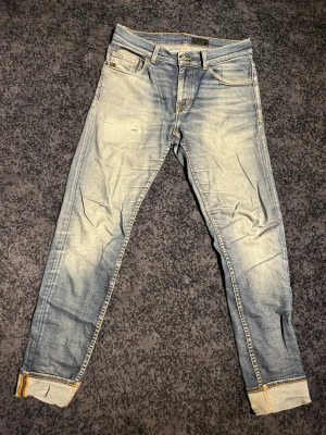 Slitna Tiger of sweden jeans  - Säljer ett par ljusblå slim fit jeans med snygg slitning och uppvikta benslut. Jeansen har klassisk femficksmodell, gul kontrastsöm och en patch bak i midjan. Perfekta för en avslappnad och trendig look. 30/32