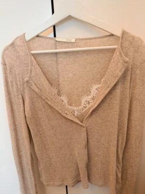 Beige kofta från zara - Mysig beige kofta från Zara  med v-ringning och knäppning framtill. Långärmad och i mjukt material, perfekt för lager på lager. Spetsdetalj syns vid halsen för en extra feminin touch.