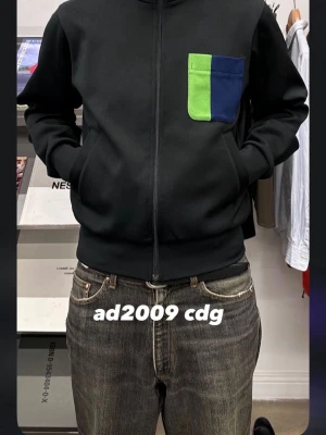 Cdg ad2009  - Svart jacka från Comme des Garçons med dragkedja framtill och en unik bröstficka i grönt och blått. 