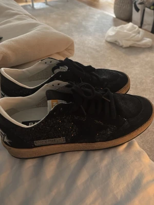 Svarta sneakers från Golden Goose - Snygga svarta sneakers från Golden Goose med glitterdetaljer och vit sula. Skorna har en stjärna på sidan och texten 'SNEAKERS' bak på hälen. Klassisk låg modell med svarta skosnören och vit insida. Nypris ungefär 6000