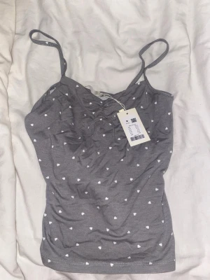 Grön linnetopp med hjärtan från lager - Supersöt  linnetopp från lager med små vita hjärtan över hela tyget. Toppen har smala axelband och en lätt rynkad detalj framtill. Perfekt att styla med jeans eller kjol för en chill look.