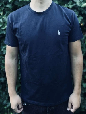 Mörkblå t-shirt från Ralph Lauren - Klassisk mörkblå t-shirt från Ralph Lauren med vit broderad logga på bröstet. T-shirten har rund halsringning och korta ärmar. Tillverkad i mjuk bomull för en skön känsla och enkel stil.