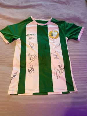 Signerad Hammarby tröja! Säsongen 2024-2025 - Säljer en officiell Hammarby IF matchtröja från Craft i klassiskt grönvitt randigt mönster. Tröjan har klubbmärke på bröstet och flera autografer på framsidan. Tillverkad i polyester med korta ärmar och rund hals. Storlek 146-152, köpte oute mindre för att det ska få plats i ram, OBS SKRIV INNAN DU KÖPER SÄLJER DEN ÄVEN PÅ BLOCKET! 