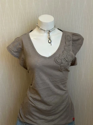 Beige topp med v-ringning och rosetter - Beige topp med v-ringning och rosetter