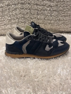 Valentino blå camo sneakers - Snygga sneakers från Valentino i blått och grått camomönster. Skorna har svarta skosnören, vit hälkappa och brun sula. Ovandelen är i mesh och mocka för en sportig och trendig look. Perfekta för dig som vill sticka ut med stil. skriv för mer info