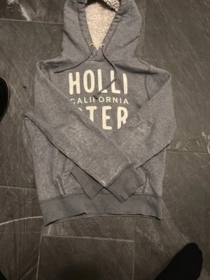 Grå hoodie från Hollister - Snygg grå hoodie från Hollister med stor vit logga på bröstet och texten 'California' vid snabb affär kan såklart priset diskuteras👍Hör av dig vid minsta lilla fundering?