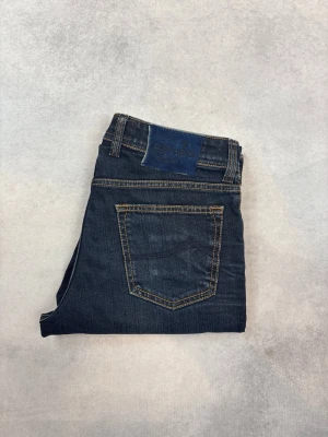 Mörkblå raka jeans från Replay - Snygga mörkblå jeans från Replay med raka ben och klassisk femficksmodell. Jeansen har kontrastsömmar och en läderpatch med logga bak i midjan. Tillverkade i slitstarkt denimtyg som ger en tidlös look.