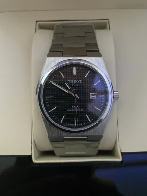 Tissot PRX - Tissot PRX herrklovka med svart urtavla, 36mm i diameter. Klockan är i nytt skick, oanvänd och funkar fint. Länkarna i armbanden kan enkelt tas bort för att korta ner och anpassa längden, just nu sitter alla länkar på. Låda med mer medföljer självklart (se bild nr 2). Hör gärna av er vid funderingar om vad som!