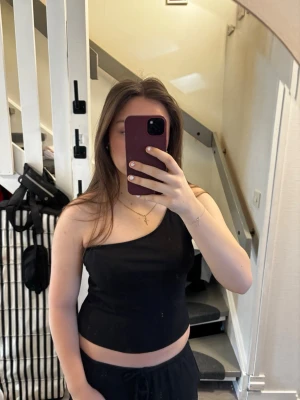 Svart oneshoulder topp - Snygg svart oneshoulder topp i stretchigt material. Toppen är croppad och har en stilren, enkel design utan synliga detaljer. Perfekt för dig som gillar minimalistisk stil och vill ha något trendigt och bekvämt.💖