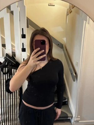 Svart oneshoulder topp - Säljer en svart långärmad topp med oneshoulder-design. Snygg och enkel modell som sitter tight och har en stilren look. Perfekt att matcha med både jeans och kjol för en trendig outfit.