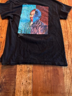 Svart Van Gogh t-shirt med tryck - Cool svart t-shirt med stort färgglatt Van Gogh-tryck på framsidan och mindre tryck på ryggen. T-shirten har klassisk passform och korta ärmar. Perfekt för dig som gillar konst och vill sticka ut med en unik design.