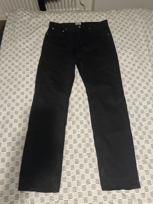 Svarta raka jeans - Svarta jeans med rak passform och klassisk femficksdesign. Jeansen har knapp- och dragkedjegylf samt bälteshällor. Perfekta för en stilren och enkel look. Storlek 34/34