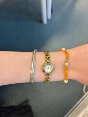 Gult pärlarmband med vita pärlor - Snyggt armband med små gula pälor och större vita pärlor som detaljer. Armbandet har ett metallspänne och är perfekt för att addera lite färg till din outfit. Passar dig som gillar unika och handgjorda accessoarer.