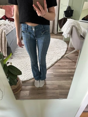 Blå bootcut jeans  - Säljer ett par blå bootcut jeans med markerade sömmar och stora fickor framtill. Jeansen har låg midja, Materialet är denim i bomull och passformen är figurnära upptill med utsvängda ben.