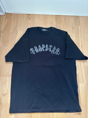 Svart Trapstar t-shirt XL - Säljer en svart t-shirt från Trapstar i storlek XL. T-shirten är NY och inte använd. Kom med förslag och tveka inte på frågor :)