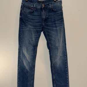 Blå jeans från Nudie Jeans - Snygga blå jeans från Nudie Jeans med klassisk femficksdesign och subtila slitningar framtill. Jeansen har raka ben och normal midja. Tillverkade i denim med tydliga kontrastsömmar och logga på bakfickan. Modell Lean Dean 