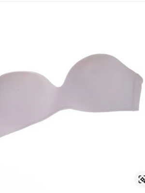 Beige axelbandslös bh - Säljer en beige axelbandslös bh med slät design och vadderade kupor. Bh:n har bygel för extra stöd och stängs med hyskor i ryggen. Perfekt under toppar utan axelband. Materialet känns mjukt och stretchigt. (Gjord av ai) det finns hoopar att sätta på egna axelband på. Ny med prislapp men köpt från Sellpy.