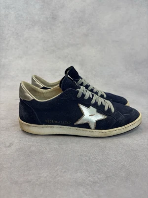 Golden Goose Ballstar blå sneakers - Snygga Ballstar sneakers från Golden Goose i mörkblå mocka med silverfärgad stjärndetalj på sidan och silverfärgad häl. Skorna har vita snören och GGDB-logga på plösen. Klassisk låg modell med vintage-inspirerad sula.