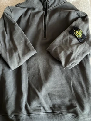 Mörkgrå Stone Island hoodie - Snygg mörkgrå hoodie från Stone Island med halv dragkedja framtill och ikonisk patch på vänster ärm.  Jag har S och den passar mig delvis lite för stor i min smak. Priset är inte hugget i sten 