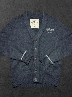 Vintage Hollister cardigan - herr strl L - Säljer en högt eftertraktad vintage Hollister cardigan i mörkgrå färg med “Hollister 1922”-brodering på bröstkorgen i storlek L  👕 Märke: Hollister 📏 Storlek: L 🎨 Färg: Mörkgrå 📍 Skick: Mycket bra skick (se bilder)  💬 Har du några frågor är det bara att höra av dig! 💰 Vid snabb affär kan priset diskuteras. 📦 Skickar alltid inom 24 timmar!