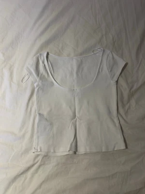 Vit croppad topp med kort ärm - En enkel och stilren vit croppad topp med korta ärmar och rundad, djup urringning. Perfekt att matcha med jeans eller kjol för en clean look. Tillverkad i mjuk bomull som känns skön mot huden.