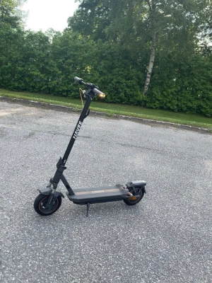Navee GT3 Elscooter - Säljer en svart elscooter från Navee med robust ram i metall och tydliga logotyper på styret och plattan. Scootern har LED-belysning fram och bak, stora hjul och en modern design med orange detaljer. Perfekt för smidig transport i stan. Den har fyrdubbelt stöddämpningssystem. Den är även bakdjulsdriven så den är väldigt enkel och rolig att stegra med.