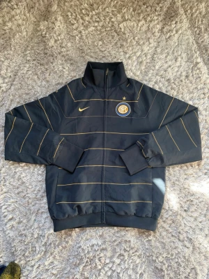 Nike Inter Milan Track suit jacka i navy/guld storlek M - ✅Hela settet finns (byxorna på profil) Snygg navy/guld vintage tracksuit jacka från Nike med Inter Milan-logga på bröstet och tunna gula linjer över hela jackan. Jackan har ykk dragkedja framtill, hög krage och ribbade muddar. Perfekt för dig som gillar fotboll och vill ha en sportig look, eller om du vill ha en skön tracksuit. Nästan nyskick, bara testad! Rekommenderas starkt