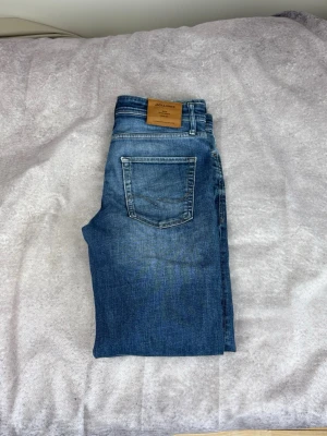Blå jeans från Jack & Jones - Säljer ett par klassiska blå jeans från Jack & Jones med fem fickor och snygga kontrastsömmar. Jeansen har en rak passform och är tillverkade i slitstarkt denimtyg. Perfekta till en avslappnad stil och funkar året runt.