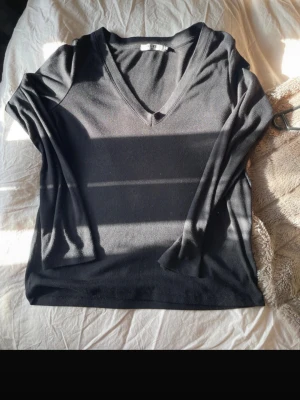 Svart ribbad v-ringad topp NA-KD - Säljer en svart långärmad topp från NA-KD med v-ringning och ribbad struktur. Perfekt basplagg som är enkel att styla till olika looks. Materialet känns mjukt och följsamt mot kroppen.