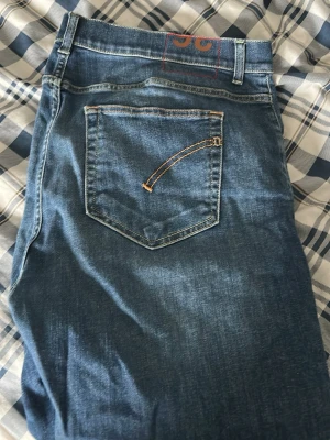 Dondup ”Alex” skinny fit - Säljer ett par klassiska blå jeans med raka ben och snygga kontrastsömmar på bakfickorna. Jeansen har en diskret logga i orange på linningen och är tillverkade i mjukt denimtyg. Perfekta för en avslappnad och trendig look.