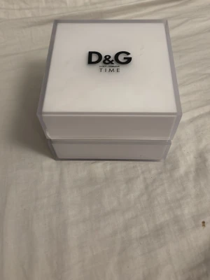 D&G silverfärgad klocka med box - Stilren klocka från D&G med fyrkantig svart urtavla och silverfärgat armband i metall. Kommer i original vit box med D&G-logga. Perfekt accessoar för dig som gillar en modern och elegant look.