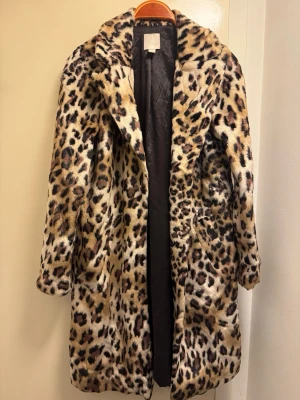Leopardmönstrad fuskpäls kappa - Snygg ofodrad och tunn leopardmönstrad kappa i fuskpäls med bred krage och två sidofickor. Kappan har en rak passform och har  svart tyg på insidan. Perfekt statement-plagg för dig som vill sticka ut. 