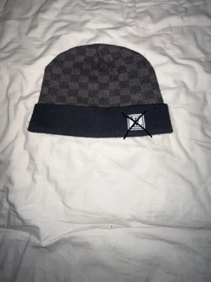 Gråmelerad mössa med rutmönster - Snygg gråmelerad mössa med diskret rutmönster och uppvikt kant. Mössan har en enkel och stilren design som passar perfekt till kalla dagar. Materialet känns mjukt och bekvämt mot huvudet. Perfekt accessoar för att hålla värmen och se cool ut. ⚠️loggan finns plick tar bort den annars