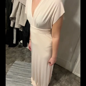 Ljusbeige omlottklänning med flera stilar - Säljer en lång ljusbeige klänning i mjukt, stretchigt tyg. Klänningen har omlottdesign och bred midjeresår, och kan stylas på flera olika sätt enligt medföljande instruktion. Perfekt för dig som vill variera din look! Klänningen har två långa band baktill som kan knytas bak, ha fallande längs ned klänningen eller knyta runt midjan!💗 jag bär vanligt vis S och är 170 lång, klänningen är lite ljusrosa, beige i färgen. 