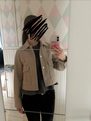 Beige vår kappa från Zara - Stilren beige overshirt från Zara i ullmix med rak, kort passform. Två stora fickor framtill med lock och tryckknappar. Klassisk krage och diskreta sömdetaljer ger en clean look. Perfekt att bära öppen eller stängd för en trendig lager-på-lager stil.