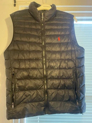 Polo Ralph lauren väst  - Köpt på Johnells för ca 3 år sedan. Väldigt sparsamt använd och i mycket bra skick  Självklart äkta  Finns två pyttesmå hål som enkelt går att fixa annars är den i toppskick och känns nästan som ny Perfekt till höst/vår Frågor funderingar det bara och skicka! 