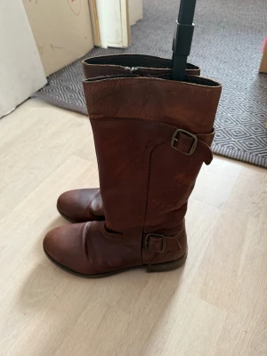 Bruna läderstövlar med spännen - Snygga och sköna bruna stövlar i äkta läder med två dekorativa spännen och dragkedja på sidan!