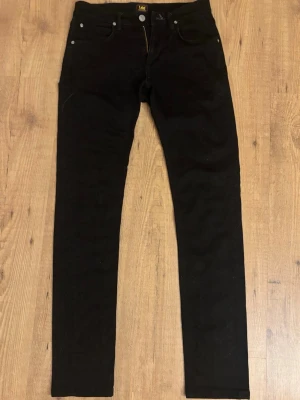 Svarta skinny Luke jeans från Lee - Säljer ett par svarta skinny Luke jeans från Lee med klassisk femficksmodell och knappgylf. Jeansen har en smal passform och är tillverkade i ett mjukt denimtyg som sitter snyggt. Perfekta för dig som gillar en stilren och enkel look.