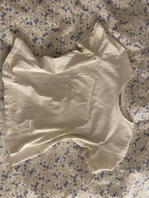 Vit topp med spetsdetalj - Söt vit topp med korta ärmar och fina spetsdetaljer vid ärmsluten. T-shirten har en enkel och stilren design, perfekt att matcha med jeans eller kjol. Den här några fläckar.